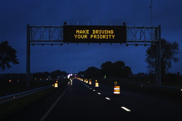 Night time "MAKE DRIVING YOUR PRIORITY" reminder caution message on an expressway.