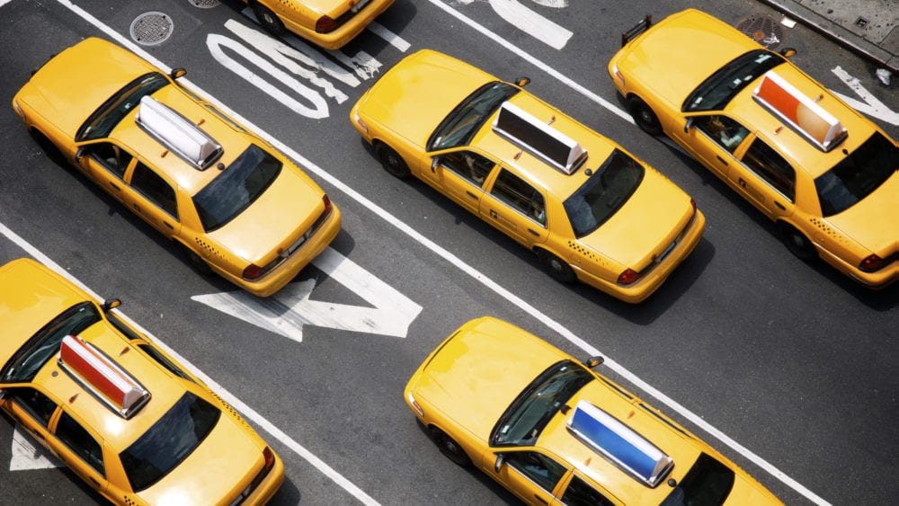 Public auto minimum liability limits, yellow taxi cabs make their way down the street of Broadway in New York City.