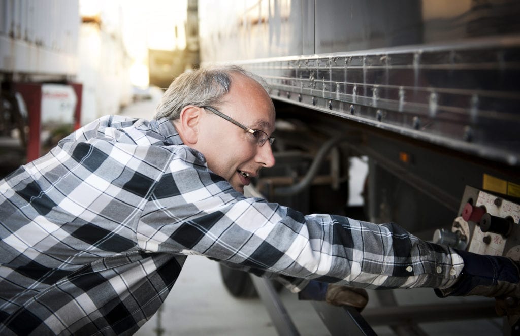 Commercial truck insurance workers compensation, truck driver checking trailer, ensuring all is properly hooked up.