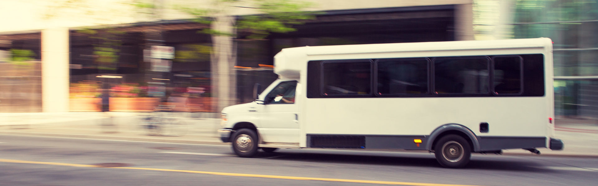 Livery insurance shuttle header, a shuttle bus driving on a city street with motion blur background.
