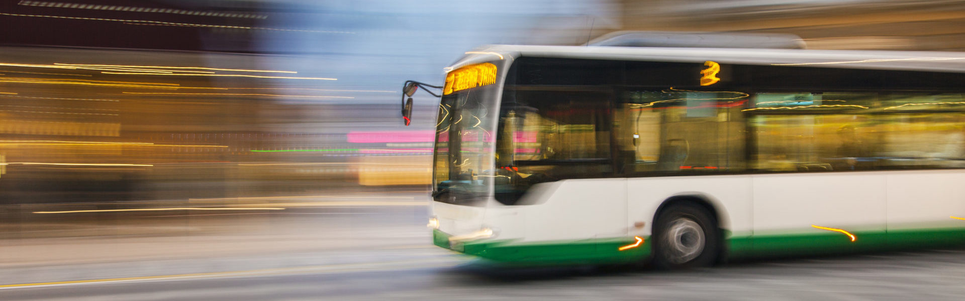 Public transportation insurance bus header, city bus driving on a city street with a motion blur background.