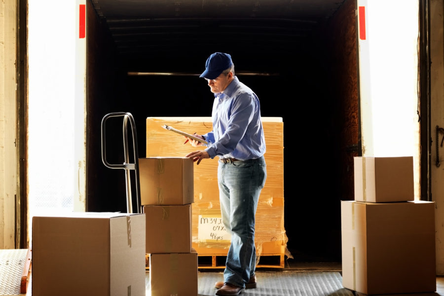 Semi truck insurance general liability, truck driver standing on loading dock, inspecting boxes.