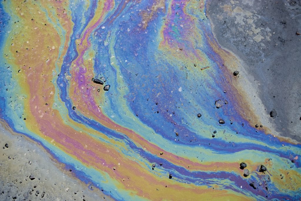 Insurance for fuel oil dealers pollution liability, cobalt blue, red, and orange oil slick on water.