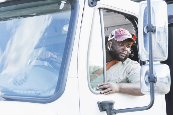 Truck driver recruiting and retention, commercial driver looks in side view mirrors while backing truck.