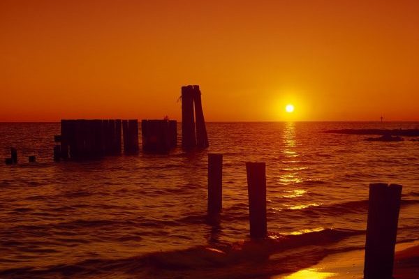 Eastern Shore of Virginia, old wharf pilings in shallow water with orange sunset in background.