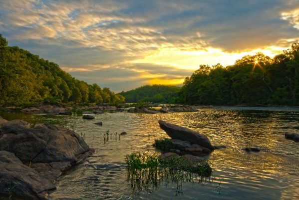 Fredericksburg, VA Rappahannock River sunrise over water, rocks, and tree-filled banks.