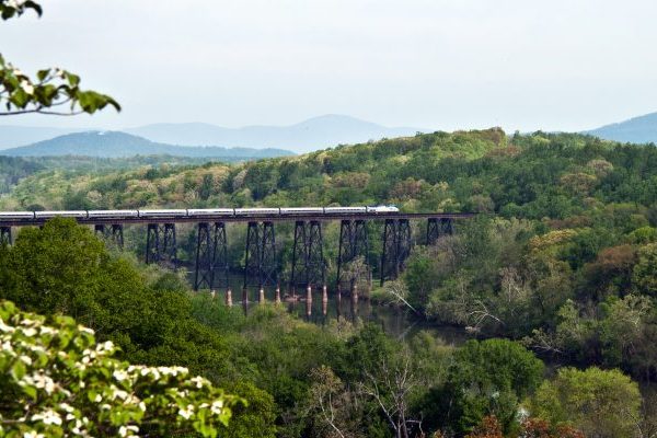 Lynchburg, VA James River Trestle train crossing high iron bridge over James River, green trees on either side of valley.