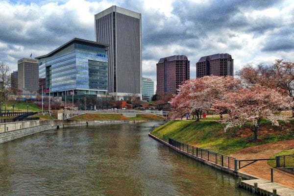 Richmond, VA canal with highrises on one side and Brown's Island on the other with green grass and budding cherry trees.