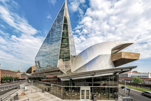 Roanoke, VA Taubman Museum of Art, a large, modern, glass, metal, and stone structure with tall glass triangular-shaped spire extending ten stories from a stainless steel sided wave-shaped structure covering a large stone-slabbed balcony overlooking surrounding city streets.