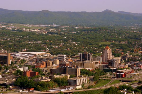 Roanoke, VA view of entire downtown area of the city, tall buildings in foreground, green mountains in background.