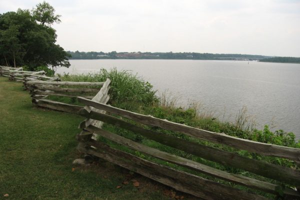 Sutherland, VA City Point, view of river from overlook of green lawn with split rail fence in foreground.