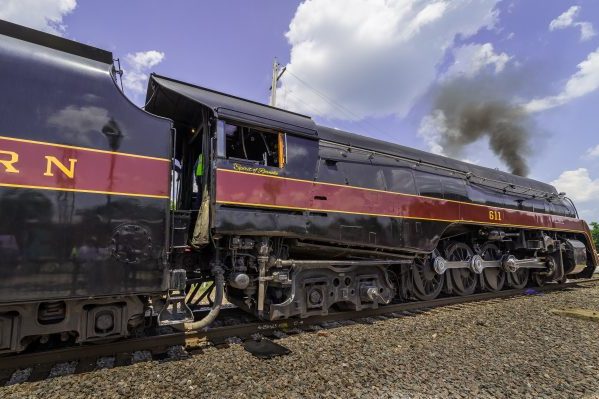 Sutherland, VA Norfolk & Western 611, closeup of sleek shiny black train engine with dark red stripe, black smoke rising against blue sky.