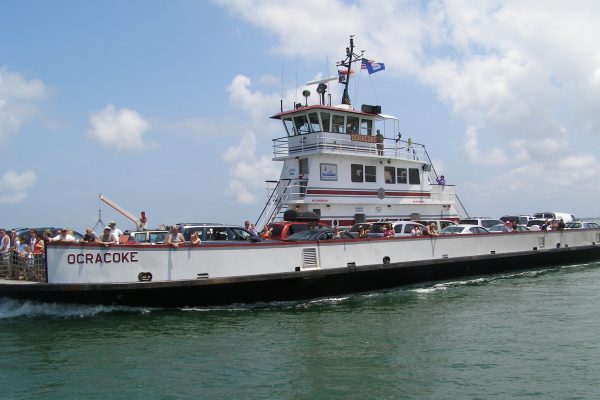 Outer Banks, NC white ferry filled with vehicles and passengers peering over sides. Vessel name is Ocracoke.
