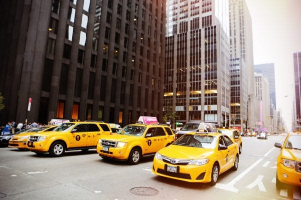 Cancellation Clause Transportation Contracts, a row of yellow taxis of all varieties, SUV and sedan, in a city with high rises in background.