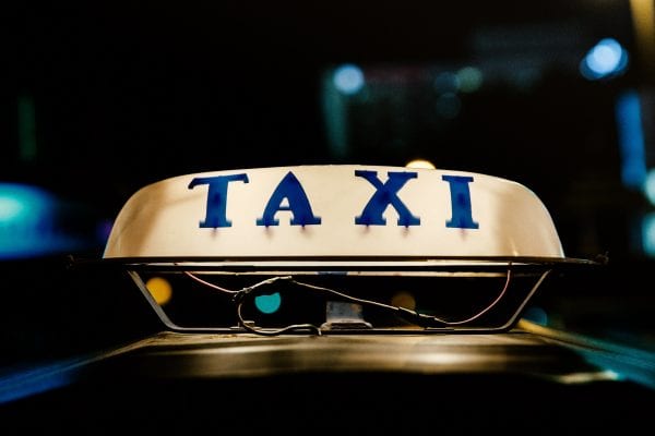 Old taxi sign atop a vehicle, lighted and at night, blue letters on white.
