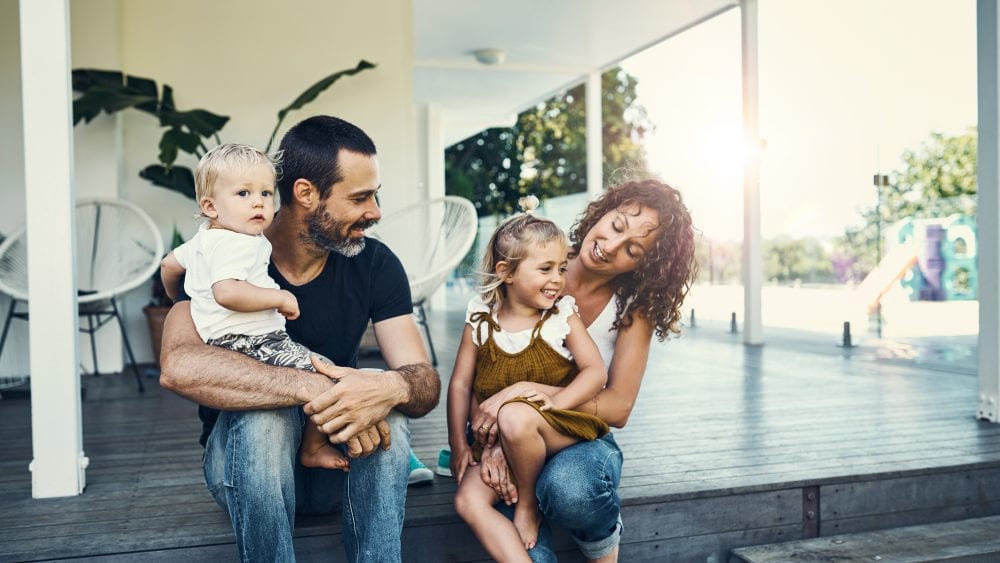 Happy young family on porch, illustrative of choosing homeowners insurance deductible.