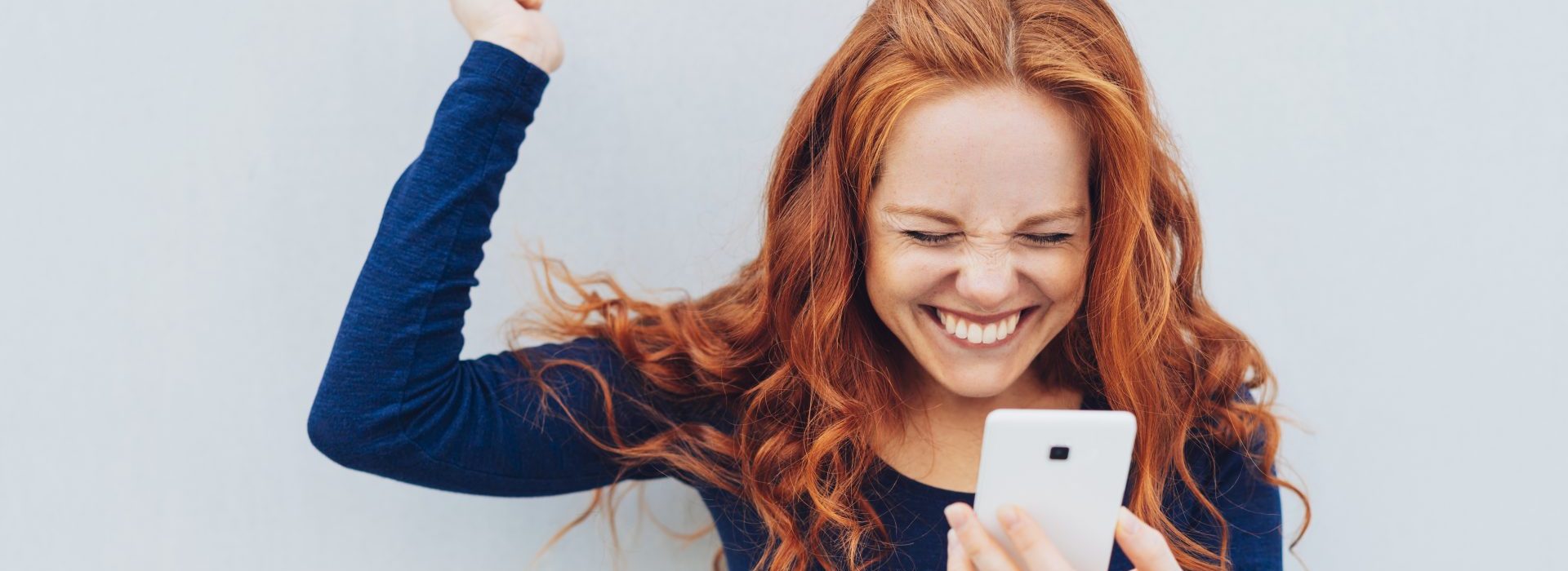 Young redhead celebrating a terrific home and car insurance quote on her mobile phone.