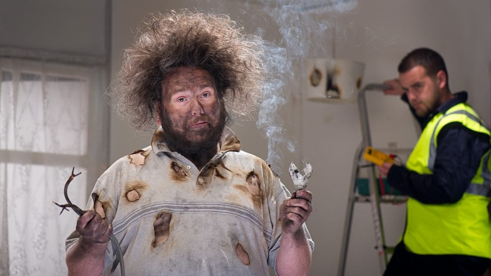 A man with burned face and frizzy hair holding smoking frayed electrical wires demonstrating common electrical wiring issues.