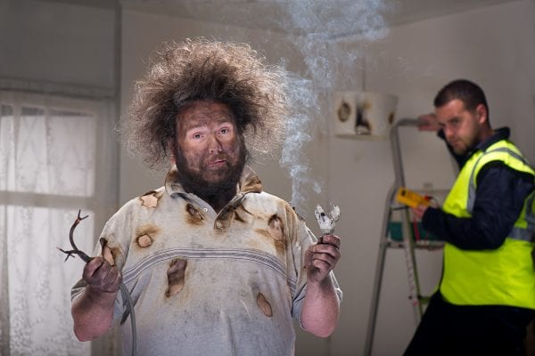 A man with burned face and frizzy hair holding smoking frayed electrical wires demonstrating common electrical wiring issues.
