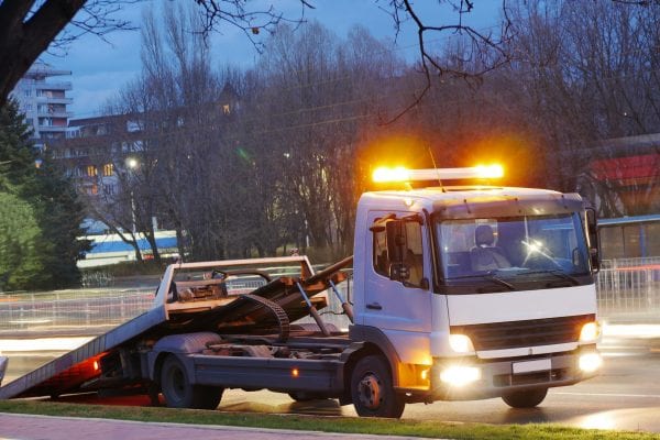 A rollback tow truck on the side of a road at dusk. Insurance pays.