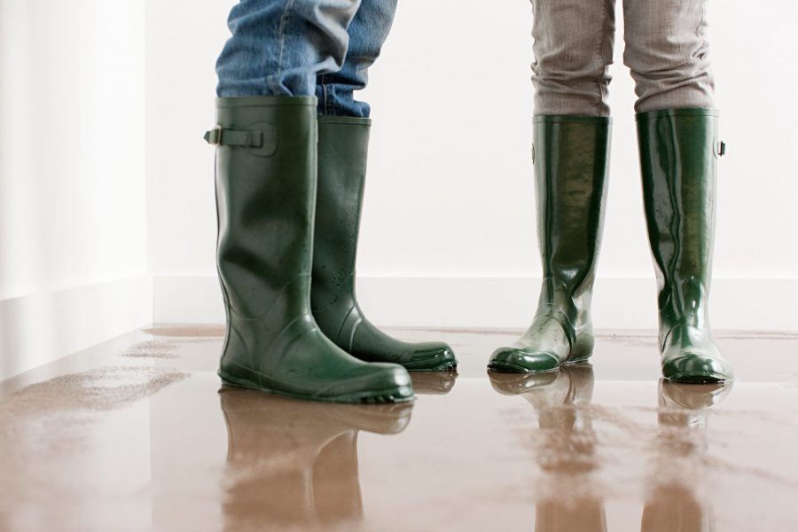 Two pair of green rubber boots on wet, flooded floor.