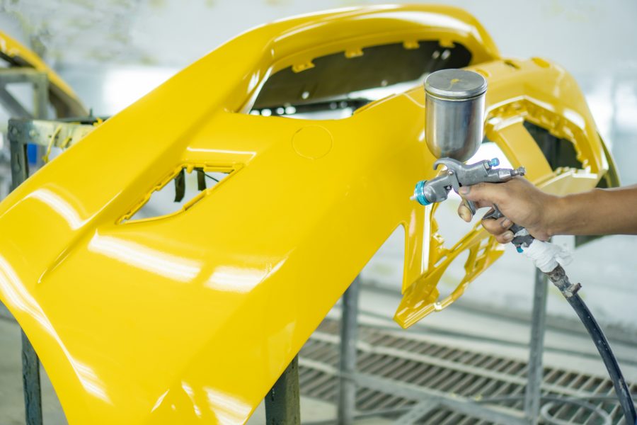 Aftermarket car bumper in a paint booth being sprayed bright yellow.