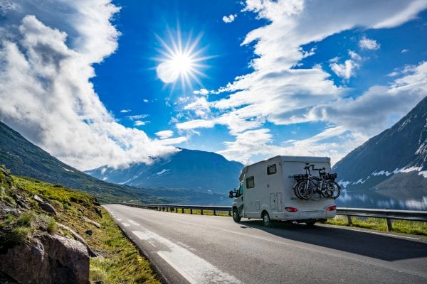 RV with bikes strapped on back on mountain road with blue sky and sunshine.