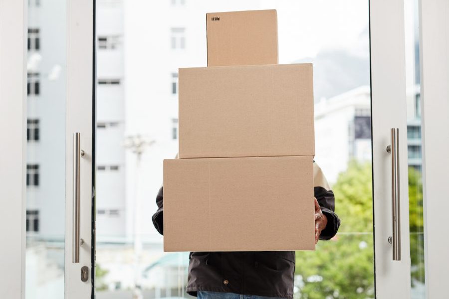 A courier with arms full of packages goes through front door of modern office.