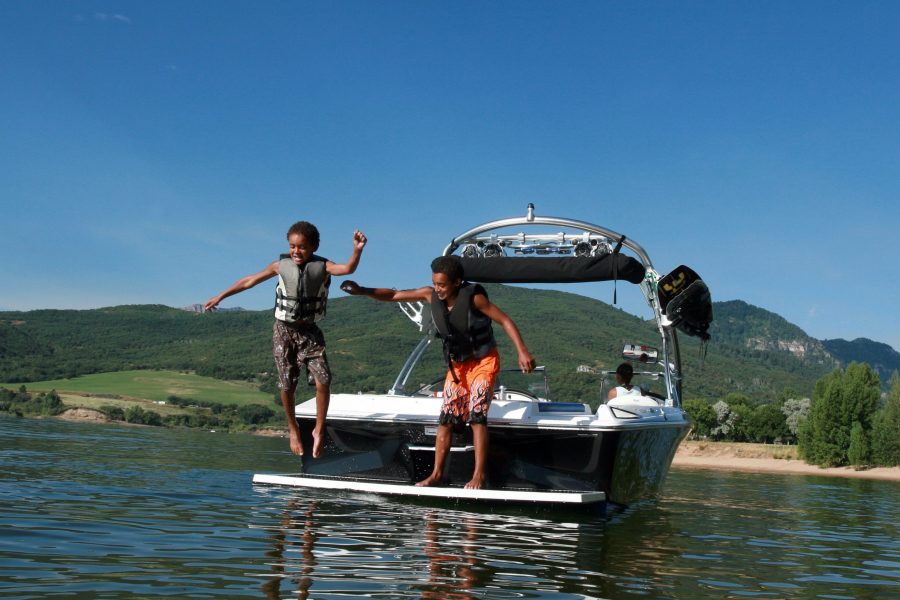 Two boys jumping into the water from the back of a motorboat, illustrating the need for boat liability insurance.